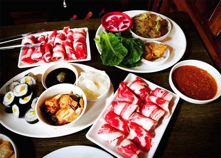 raw samgyupsal, kimbap, kimchi, japchae, and samjang 