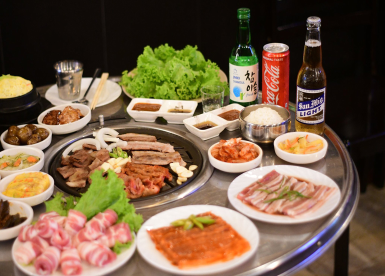 Assortments of meat cuts, side dishes, and beverages such as beer, soju, and coke
