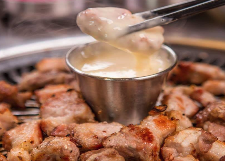 Samgyupsal dipped in creamy cheese with chopsticks