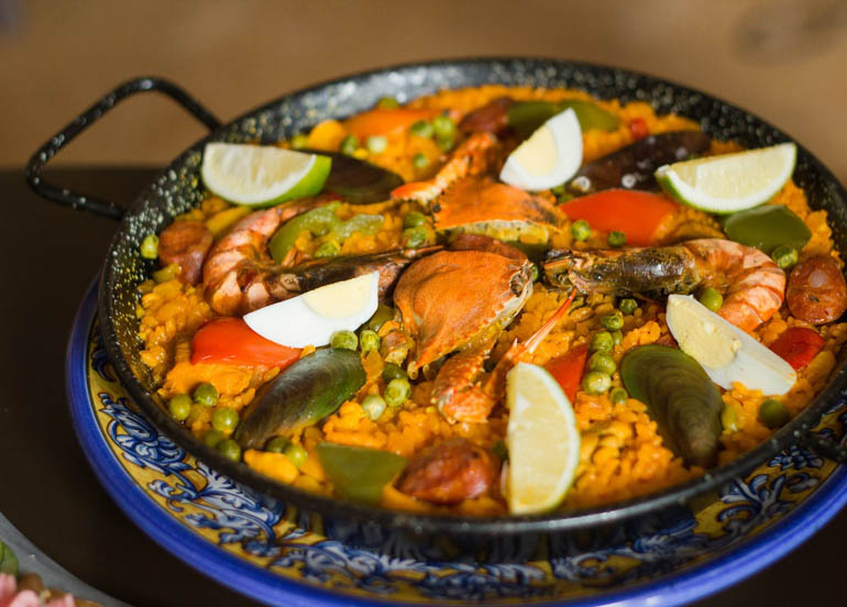 Paella Valenciana from Alba topped with egg, shrimps, lime, shellfish, seafood, and peas