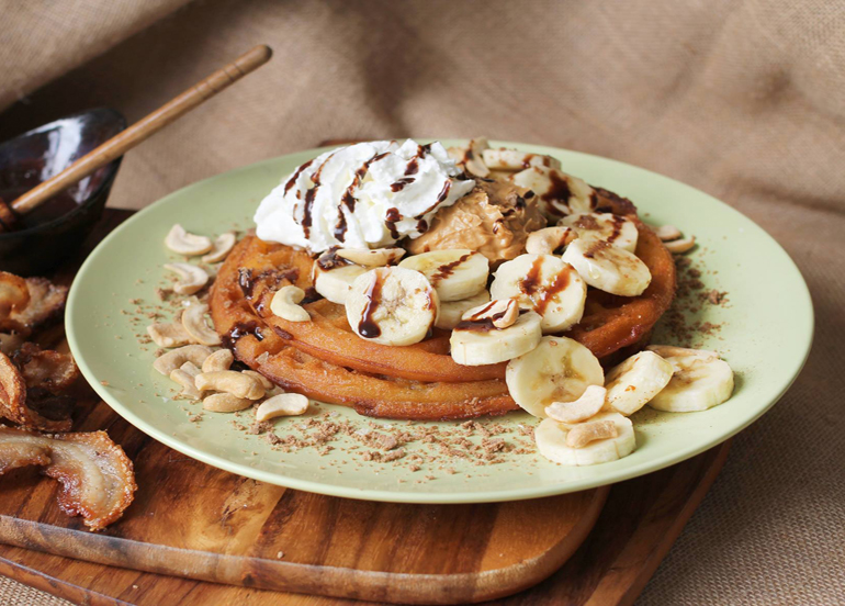 Tsokolateria Waffle topped with banana, whipped cream, and chocolate syrup